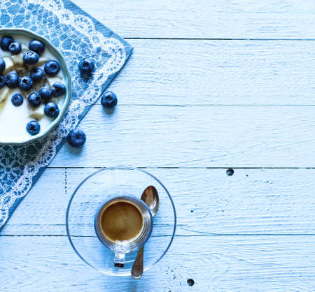 Healthy Breakfast with blueberries and banana yogurt, biscuits, marmalade, coffee and peaches over a light wooden background.の写真素材