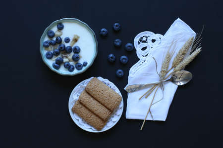 Healthy Breakfast with blueberries and banana yogurt, biscuits, marmalade, coffee and peaches over a light wooden background.の写真素材