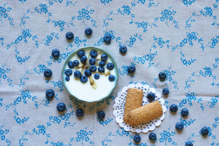 Healthy Breakfast with blueberries and banana yogurt, biscuits, marmalade, coffee and peaches over a light wooden background.の写真素材
