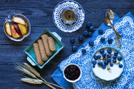 Healthy Breakfast with blueberries and banana yogurt, biscuits, marmalade, coffee and peaches over a light wooden background.の写真素材