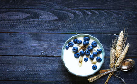 Healthy Breakfast with blueberries and banana yogurt, biscuits, marmalade, coffee and peaches over a light wooden background.の写真素材