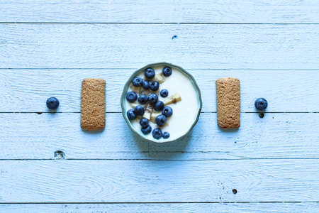 Healthy Breakfast with blueberries and banana yogurt, biscuits, marmalade, coffee and peaches over a light wooden background.の写真素材