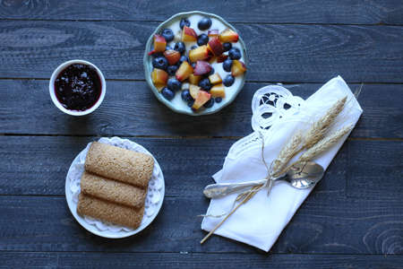 Healthy Breakfast with blueberries and banana yogurt, biscuits, marmalade, coffee and peaches over a light wooden background.の写真素材