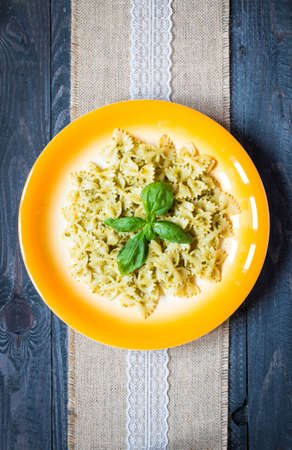 Italian pasta with pesto sauce made with basil leafs, pine nuts, fresh garlic and olive oil over an old wood background, top viewの写真素材