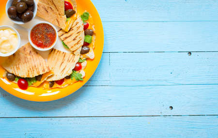 Delicious veggie quesadillas with tomatoes, olives, saòad and cheddar cheese in a colorful dish over a woodenの写真素材