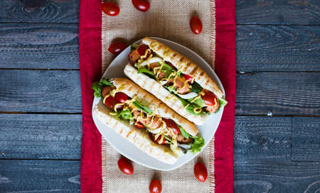 Hot dog with pickles, tomatoes, olives and lettuce  on wooden background. Top viewの写真素材