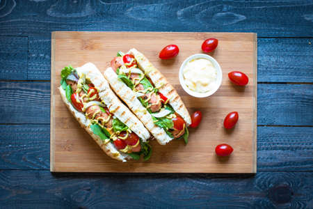 Hot dog with pickles, tomatoes, olives and lettuce  on wooden background. Top viewの写真素材