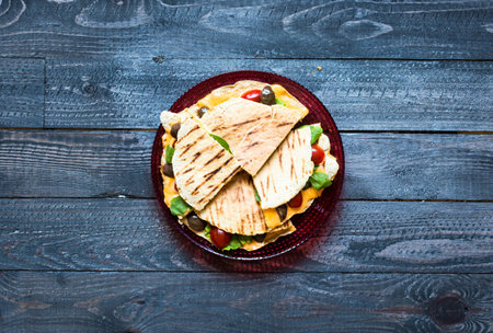 Delicious veggie quesadillas with tomatoes, olives, saòad and cheddar cheese in a colorful dish over a woodenの写真素材