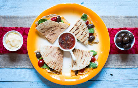 Delicious veggie quesadillas with tomatoes, olives, saòad and cheddar cheese in a colorful dish over a woodenの写真素材