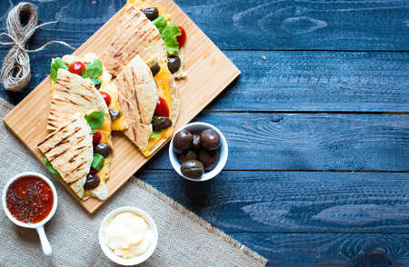 Delicious veggie quesadillas with tomatoes, olives, saòad and cheddar cheese in a colorful dish over a woodenの写真素材