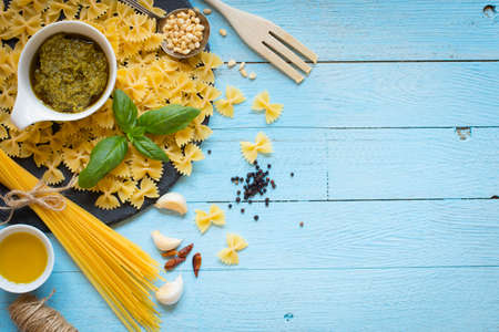 Italian pasta with pesto sauce made with basil leafs, pine nuts, fresh garlic and olive oil over an old wood background, top viewの写真素材