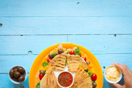 Delicious veggie quesadillas with tomatoes, olives, saòad and cheddar cheese in a colorful dish over a woodenの写真素材