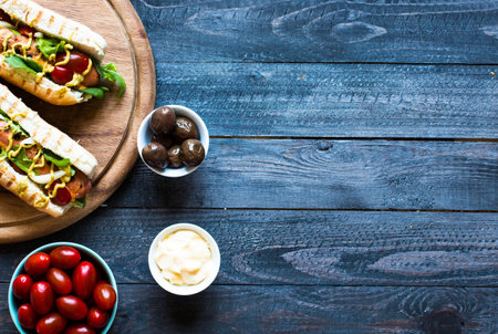 Hot dog with pickles, tomatoes, olives and lettuce  on wooden background. Top view