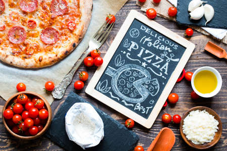 Hot Italian pizza with melting tomato,pepperoni and cheese on a rustic wooden table.の写真素材