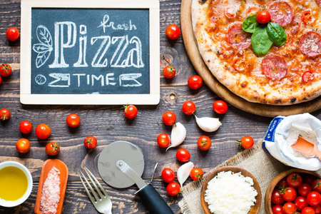 Hot Italian pizza with melting tomato,pepperoni and cheese on a rustic wooden table.の写真素材