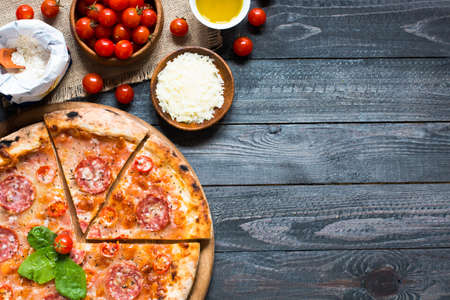 Hot Italian pizza with melting tomato,pepperoni and cheese on a rustic wooden table.の写真素材
