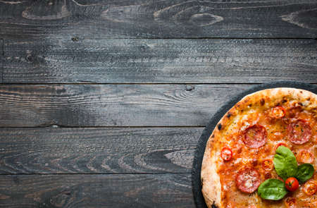 Hot Italian pizza with melting tomato,pepperoni and cheese on a rustic wooden table.の写真素材