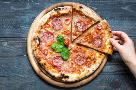 Hot Italian pizza with melting tomato,pepperoni and cheese on a rustic wooden table.の写真素材