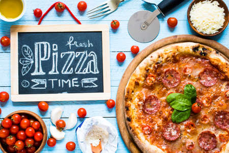 Hot Italian pizza with melting tomato,pepperoni and cheese on a rustic wooden table.の写真素材