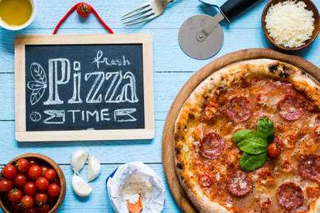 Hot Italian pizza with melting tomato,pepperoni and cheese on a rustic wooden table.の写真素材