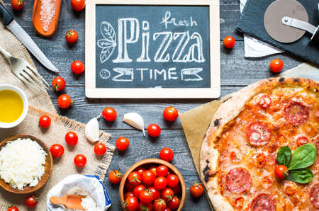 Hot Italian pizza with melting tomato,pepperoni and cheese on a rustic wooden table.の写真素材