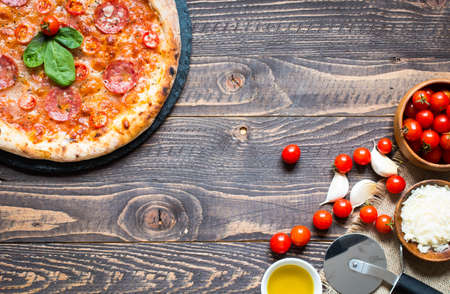 Hot Italian pizza with melting tomato,pepperoni and cheese on a rustic wooden table.の写真素材