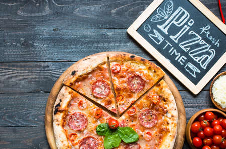 Hot Italian pizza with melting tomato,pepperoni and cheese on a rustic wooden table.の写真素材