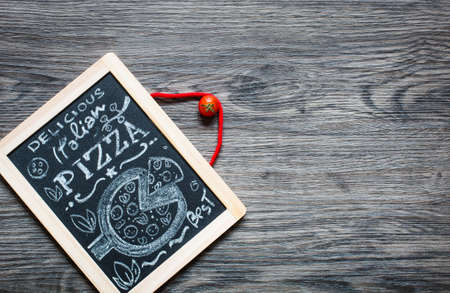 Poster with pizza stylized chalk inscription and drawing on a blackboard over an old wooden table.の写真素材