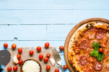 Hot Italian pizza with melting tomato,pepperoni and cheese on a rustic wooden table.の写真素材