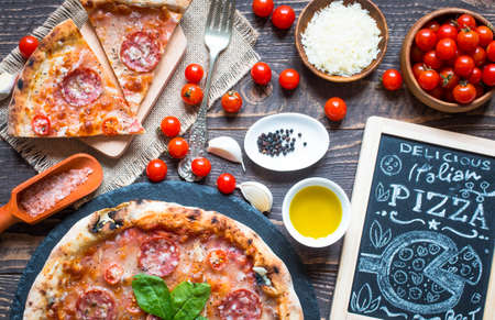 Hot Italian pizza with melting tomato,pepperoni and cheese on a rustic wooden table.の写真素材