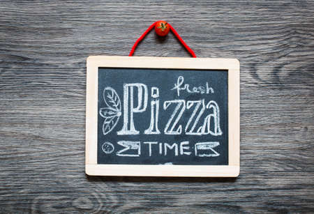 Poster with pizza stylized chalk inscription and drawing on a blackboard over an old wooden table.の写真素材