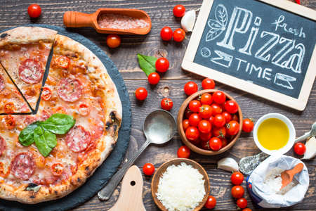 Hot Italian pizza with melting tomato,pepperoni and cheese on a rustic wooden table.の写真素材