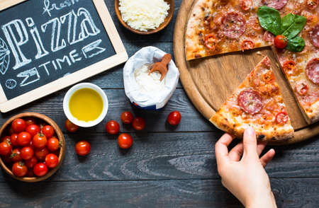 Hot Italian pizza with melting tomato,pepperoni and cheese on a rustic wooden table.の写真素材