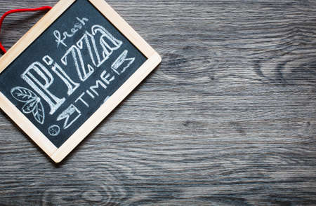 Poster with pizza stylized chalk inscription and drawing on a blackboard over an old wooden table.の写真素材