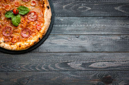 Hot Italian pizza with melting tomato,pepperoni and cheese on a rustic wooden table.の写真素材