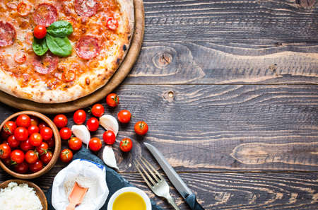 Hot Italian pizza with melting tomato,pepperoni and cheese on a rustic wooden table.の写真素材