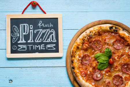 Hot Italian pizza with melting tomato,pepperoni and cheese on a rustic wooden table.