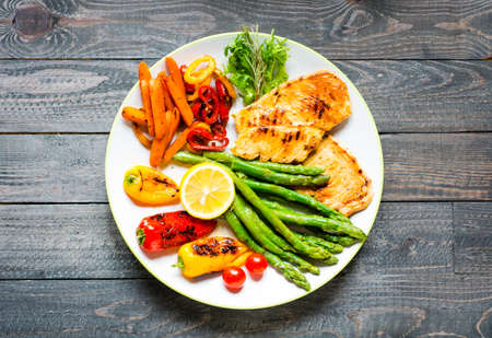 Grilled chicken breast with fresh vegetables on wooden backgroundの写真素材