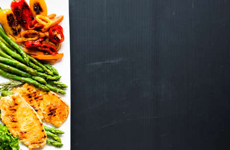 Grilled chicken breast with fresh vegetables on a black woodの写真素材