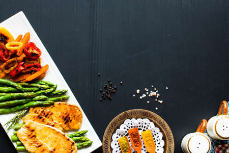 Grilled chicken breast with fresh vegetables on a black woodの写真素材