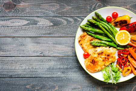 Grilled chicken breast with fresh vegetables on wooden backgroundの写真素材