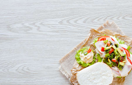 Fresh and tasty sandwich with ham and vegetables, isolated and tomato on wooden backgroundの写真素材