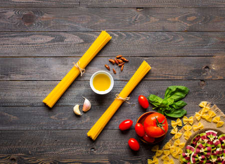 Pasta background. Several types of dry pasta with vegetables,and herbs. On a wooden table. Free space for text . Top viewの写真素材