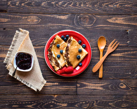 Fresh Strawberries Pancakes or Crepes with berries and chocolate over a wooden tableの写真素材