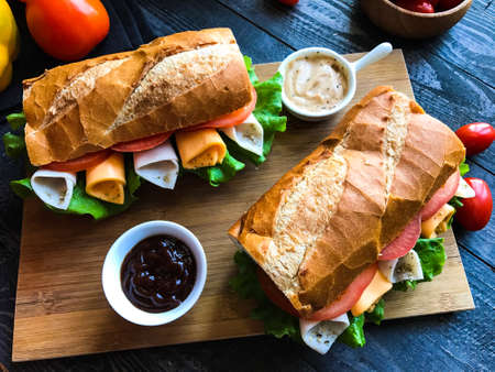 Delicious and Tasty sandwiches with turkey, ham, cheese, tomatoes and salad over a wooden table full of fresh vegetables.の写真素材