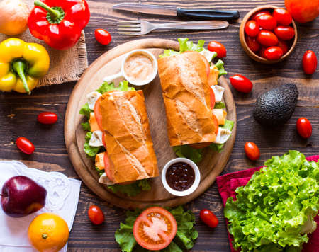 Delicious and Tasty sandwiches with turkey, ham, cheese, tomatoes and salad over a wooden table full of fresh vegetables.の写真素材