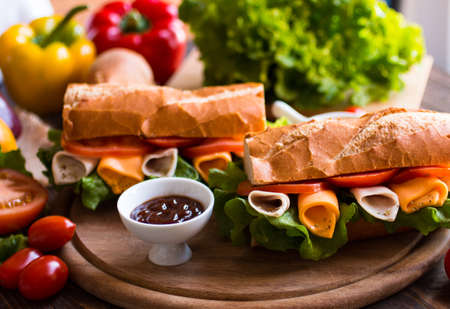 Delicious and Tasty sandwiches with turkey, ham, cheese, tomatoes and salad over a wooden table full of fresh vegetables.の写真素材