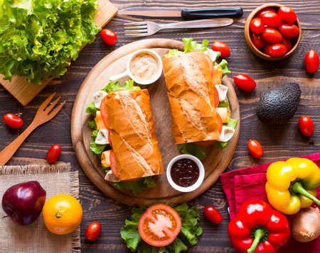 Delicious and Tasty sandwiches with turkey, ham, cheese, tomatoes and salad over a wooden table full of fresh vegetables.の写真素材