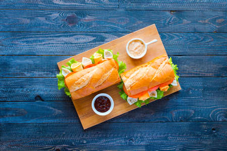 Delicious and Tasty sandwiches with turkey, ham, cheese, tomatoes and salad over a wooden table full of fresh vegetables.の写真素材
