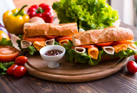 Delicious and Tasty sandwiches with turkey, ham, cheese, tomatoes and salad over a wooden table full of fresh vegetables.の写真素材